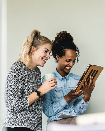Zwei Studentinnen lachen und schauen auf ein Tablet